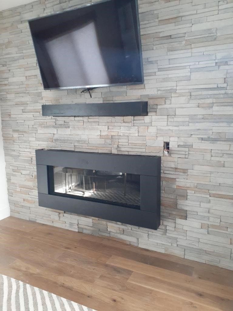 Modern living room wall with mounted TV above a black fireplace and stone veneer backdrop, wood floor below