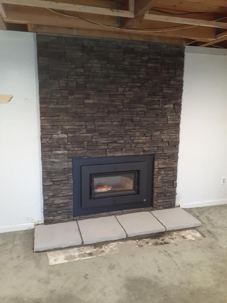 Stone-faced fireplace with black insert under a covered patio, framed by white walls and concrete pavers.