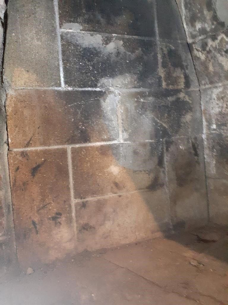 Dirty brick wall and floor corner with soot stains and scattered debris.