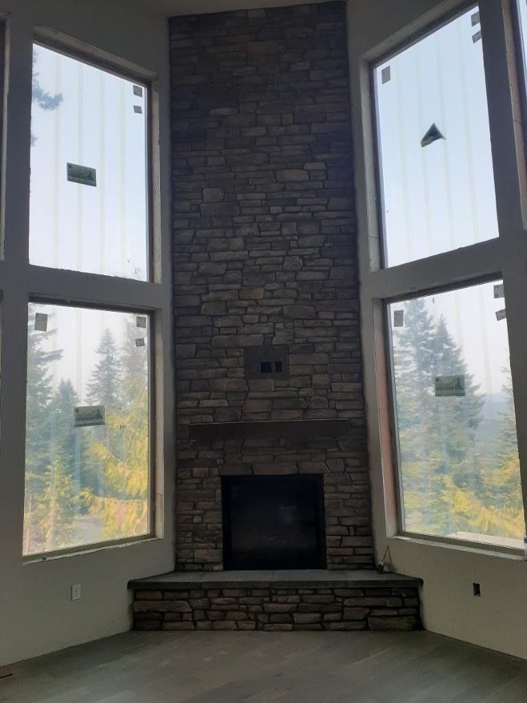 Tall stone fireplace with large windows on both sides in a bright living room.