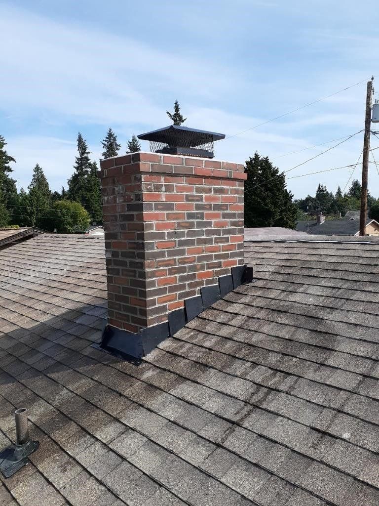 Brick chimney on a shingled roof under a clear blue sky.