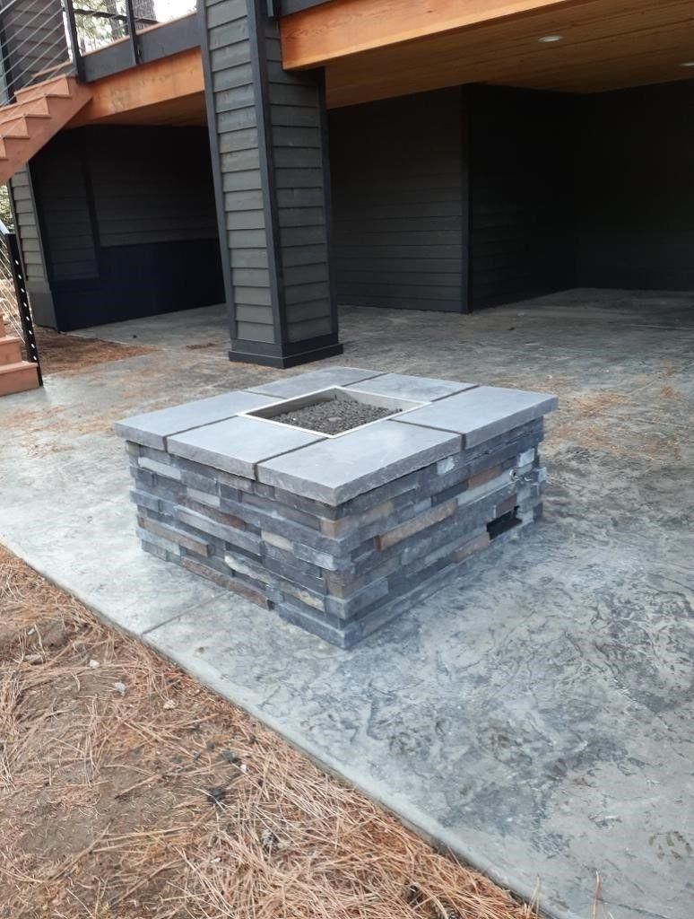 Stone fire pit on a concrete patio beside a house and open garage.