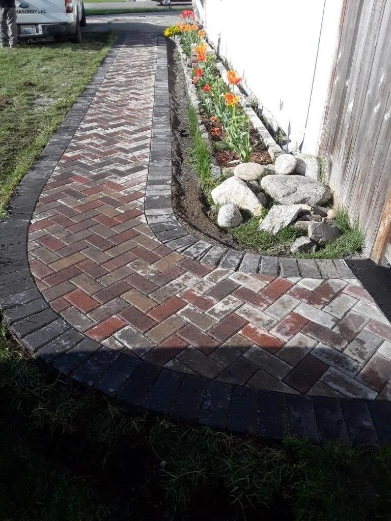 Curved brick garden path beside a white fence with flowers and rocks along the edge