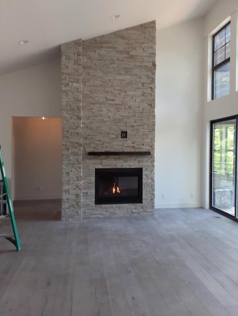Modern living room with a stone fireplace, tall windows, and a ladder on the left.