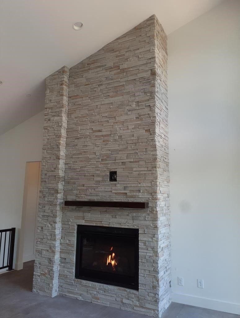Modern living room fireplace with tall stacked-stone surround and a lit fire.
