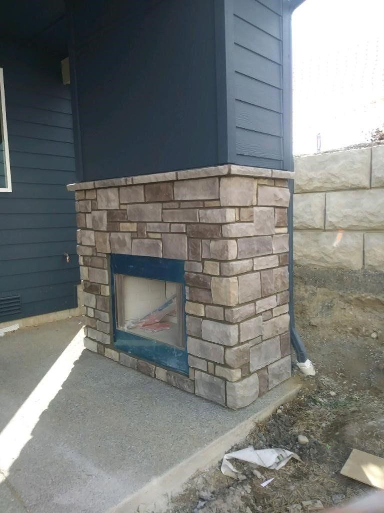 Stone-clad outdoor fireplace attached to a dark blue house beside a concrete patio