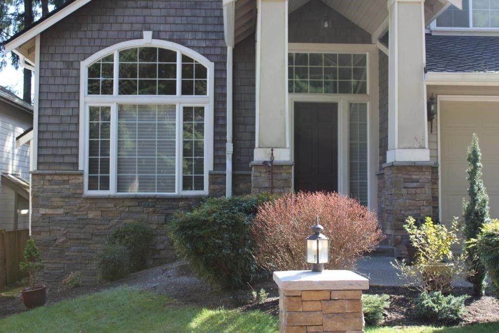 Front entrance of a stone house with arched window, front door, shrubs, and a brick mailbox in the yard