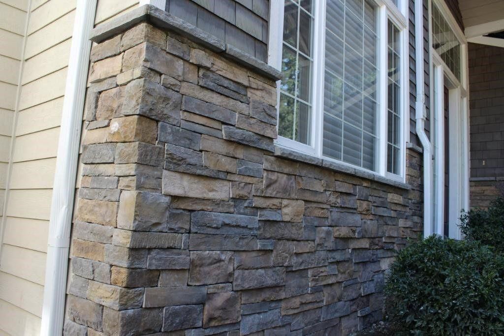 Stone and beige siding on a house exterior with a window and shrubbery