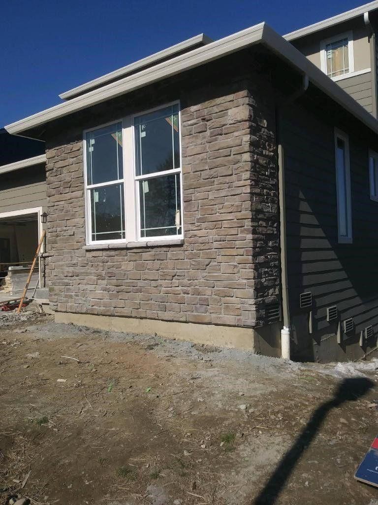 Stone-sided house exterior with large window and unfinished dirt yard