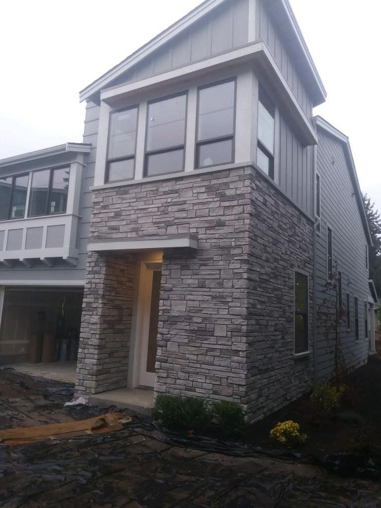 Modern two-story house exterior with stone veneer, gray siding, and a front entry porch