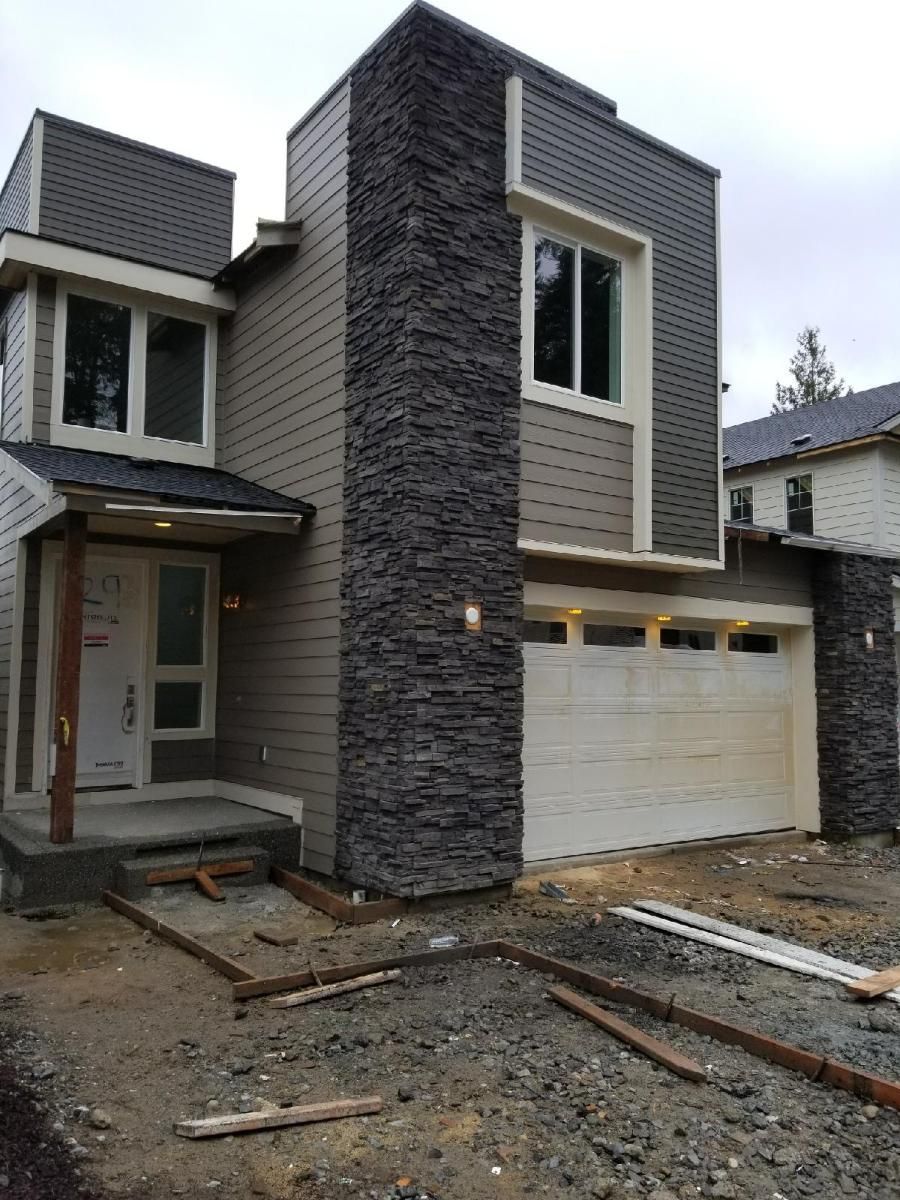 Modern two-story house exterior with stone column and unfinished front yard, garage on the right