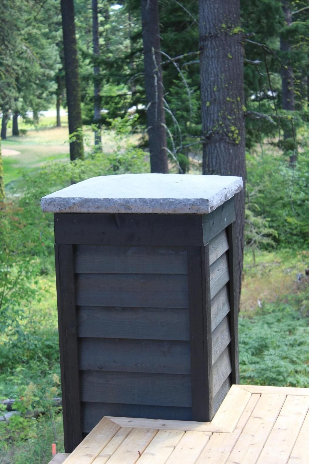 Dark wooden deck post with snow-covered cap in a wooded outdoor setting