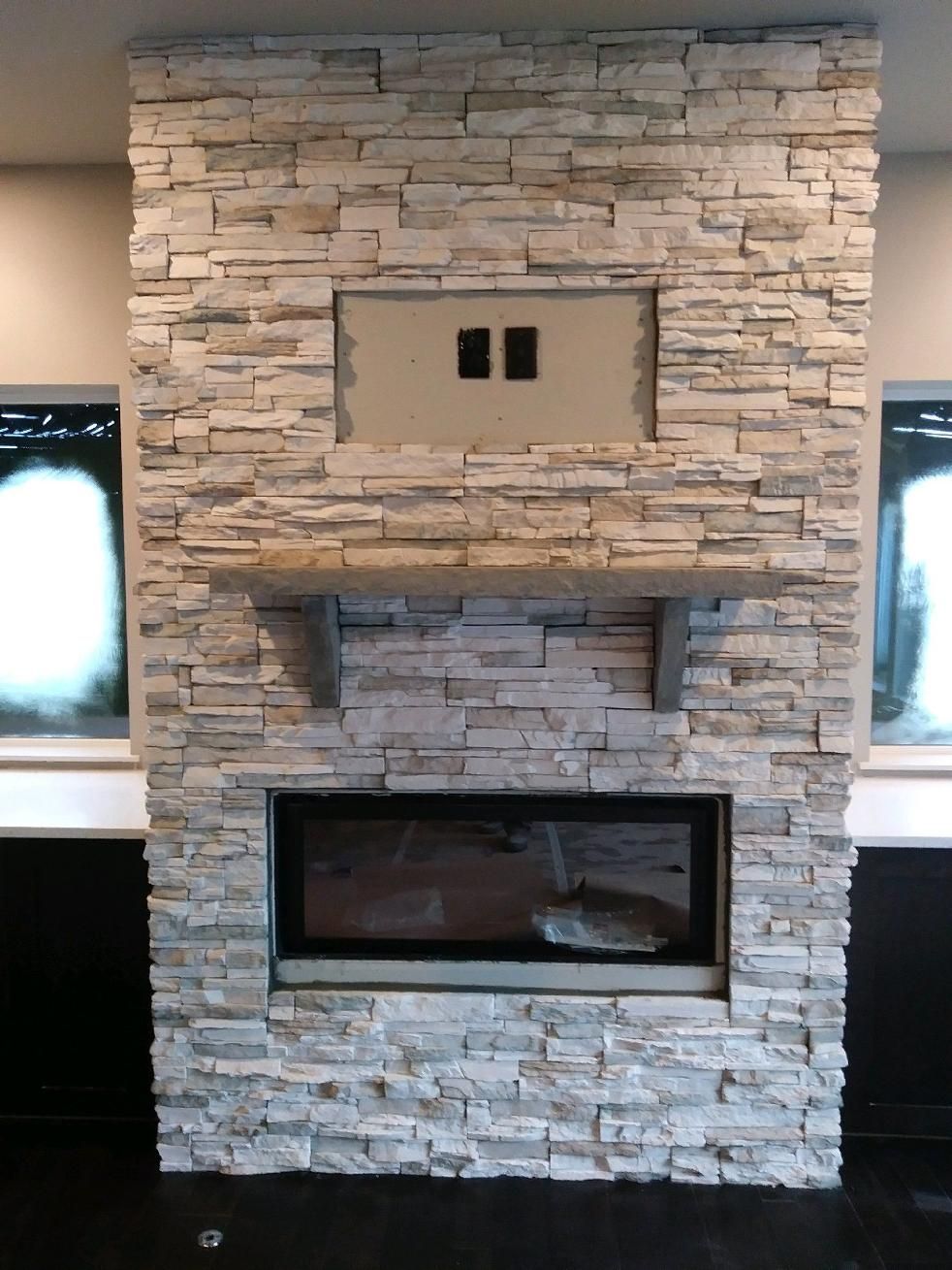 Stone-faced fireplace with a built-in TV niche above and a large firebox below, framed by two windows.