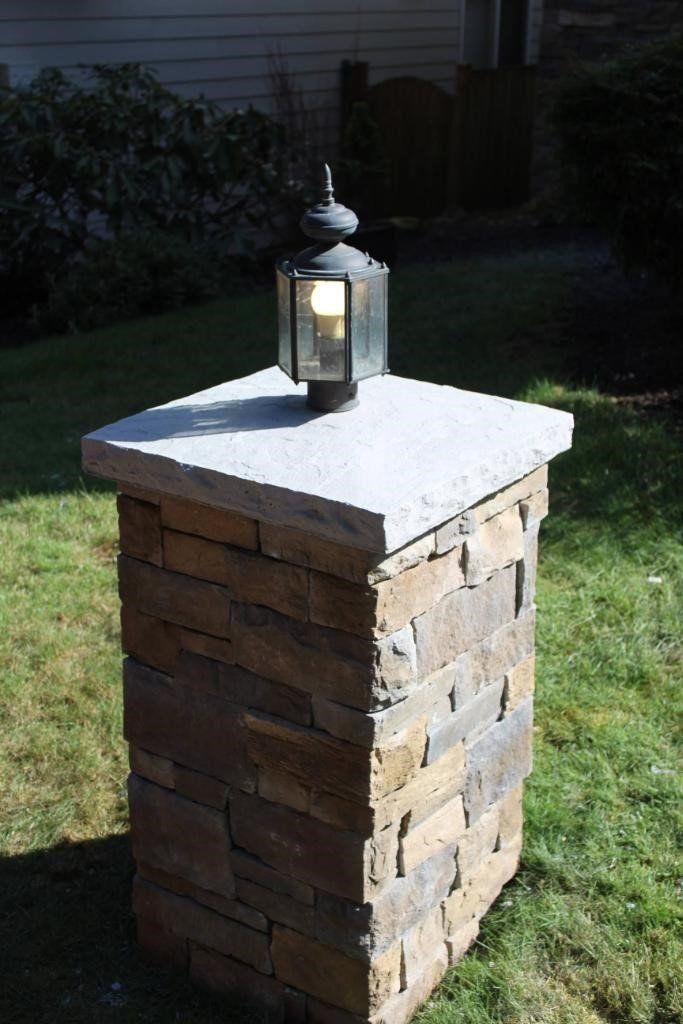 Stone garden pedestal with a lantern on top on a grassy lawn at dusk