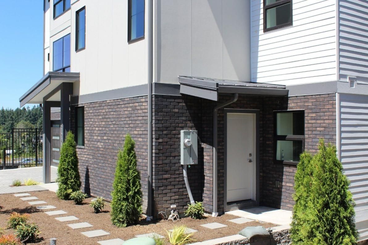 Modern house entrance with stone siding, white walls, and small shrubs by the door