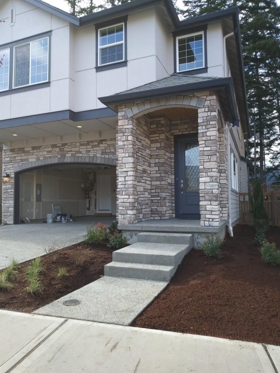Front entrance of a townhouse with stone columns, a garage, and a short concrete walkway leading to the door