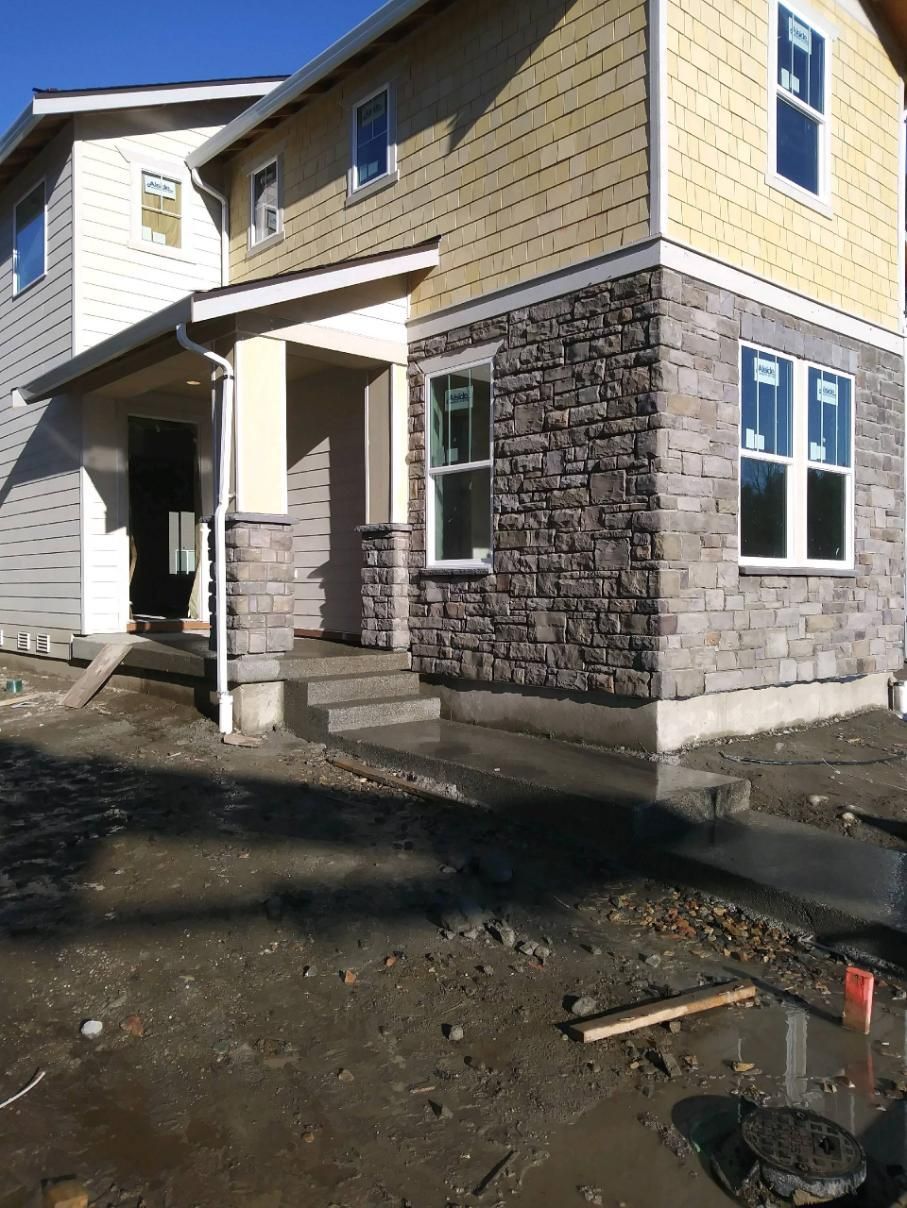 New beige and stone house exterior with unfinished dirt yard and front porch
