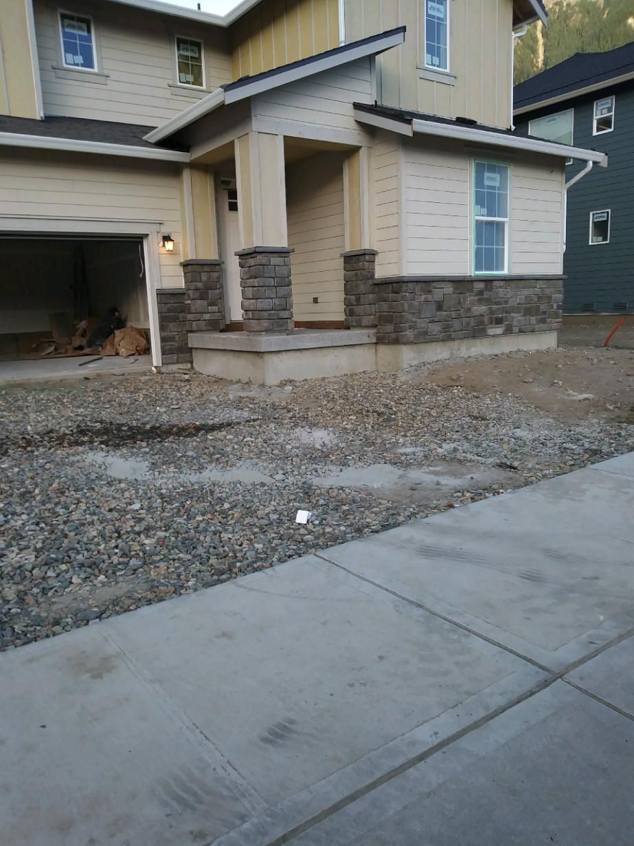 Suburban house exterior with unfinished gravel driveway and concrete sidewalk in front of garage