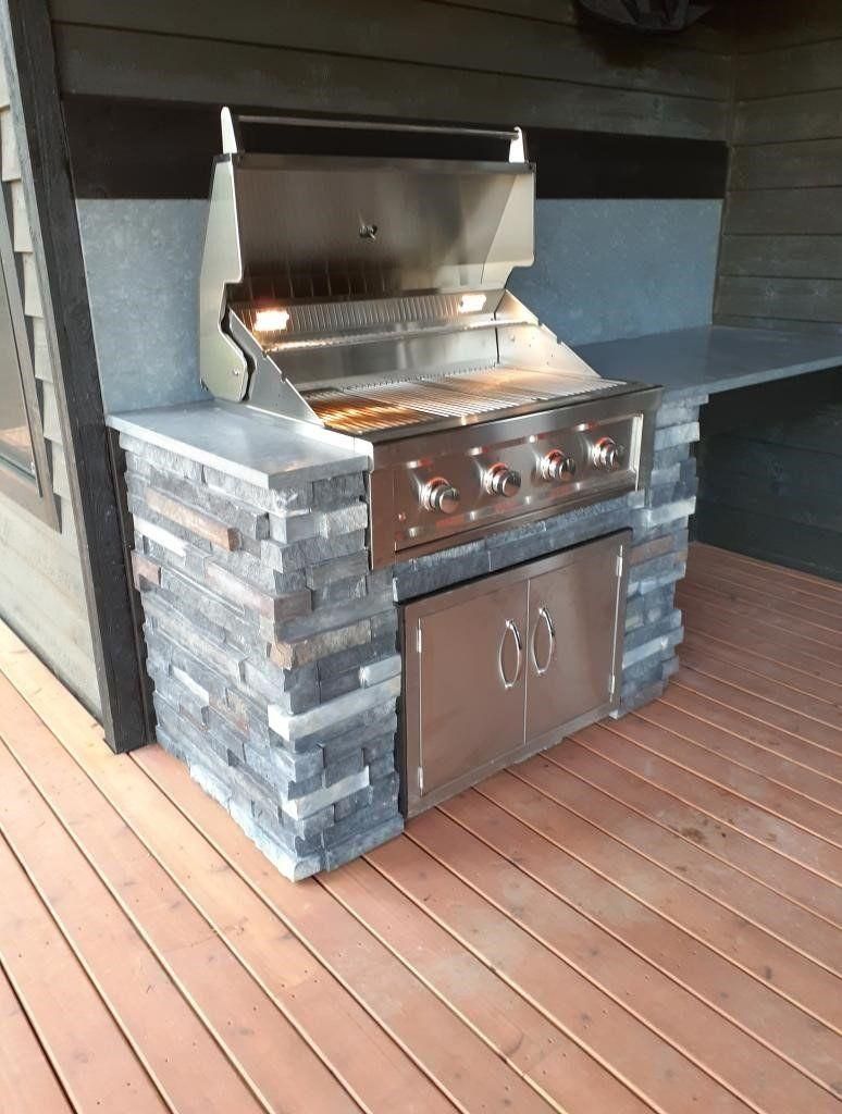 Outdoor stainless steel grill built into a stone base on a wooden deck