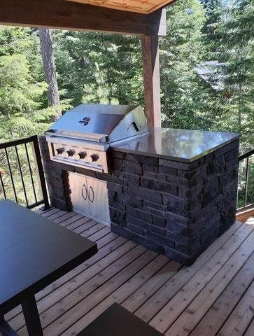 Covered wooden deck with a stainless steel grill and black stone outdoor kitchen overlooking forest trees