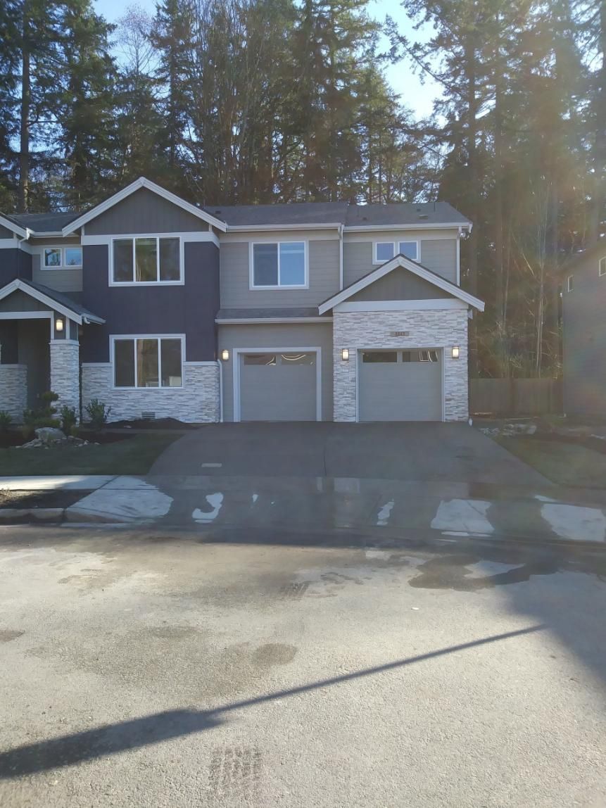 Two-story townhouse with attached garages, fronted by a paved driveway and tall trees behind.