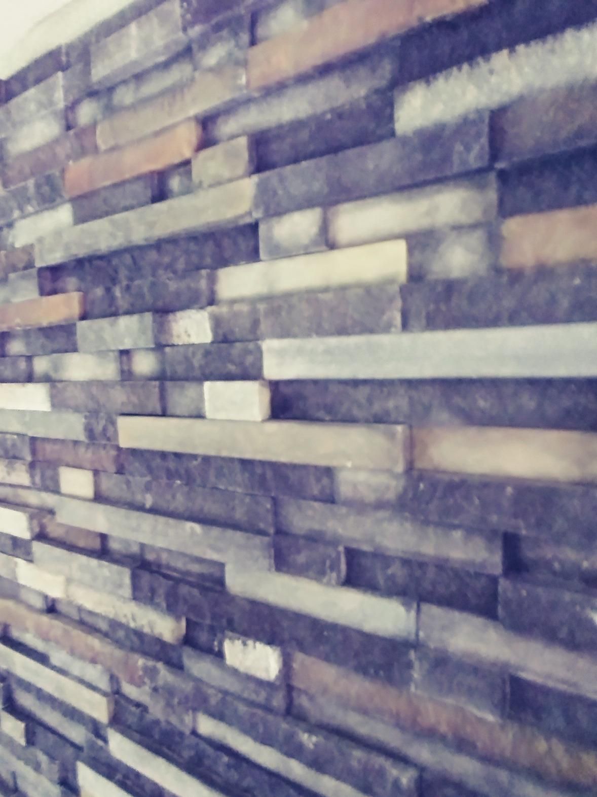 Close-up of a stacked stone wall with gray, beige, and white rectangular tiles.