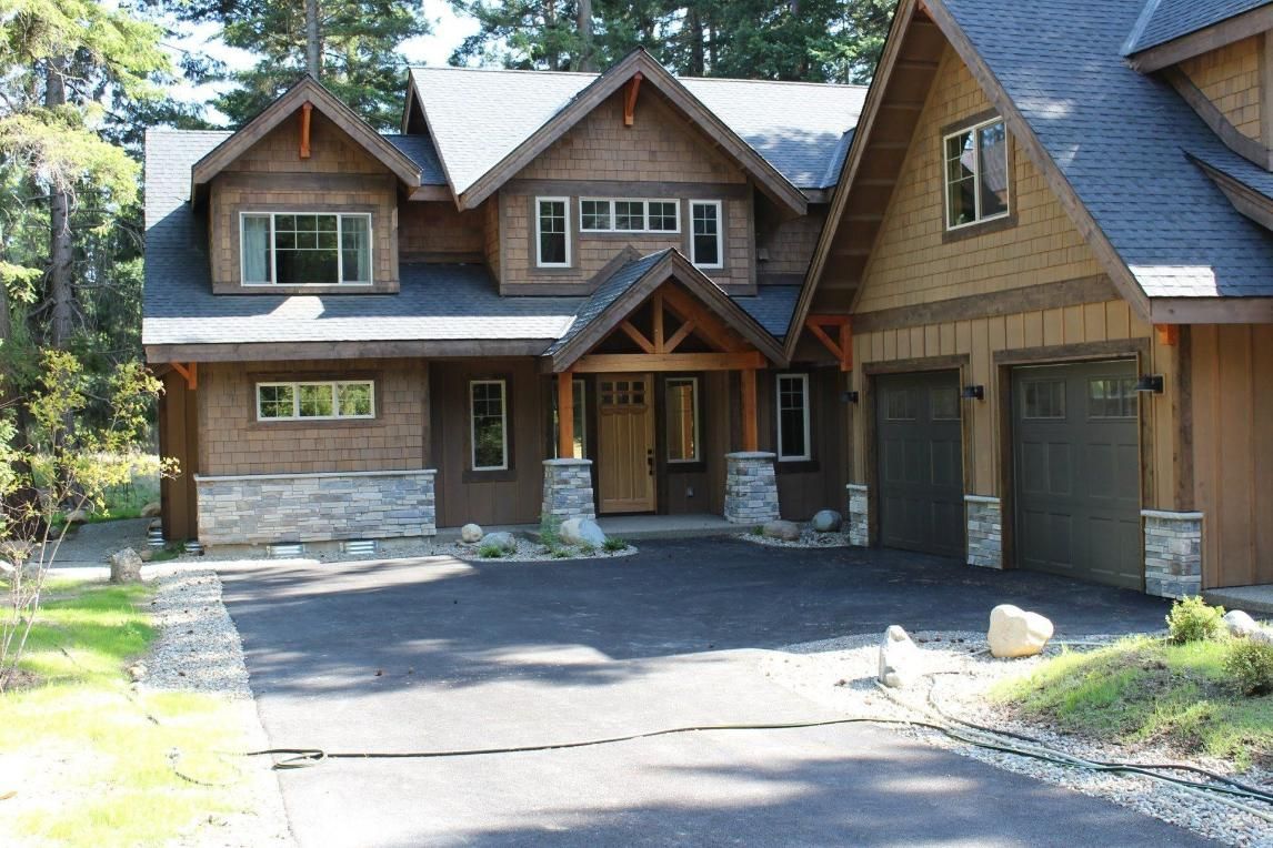 Large rustic house with stone and wood siding, driveway, and two-car garage in a wooded setting