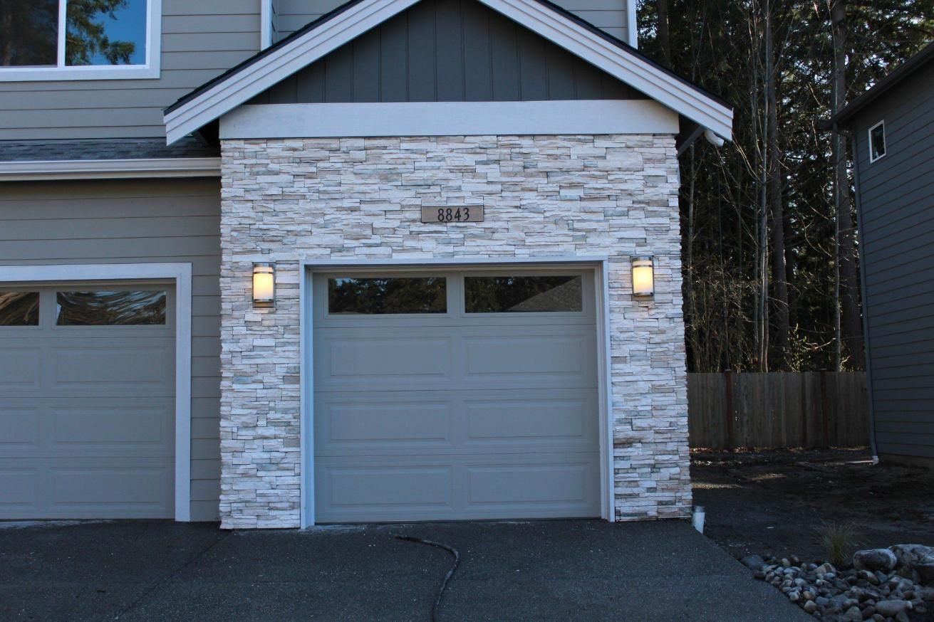 House exterior with stone veneer and two gray garage doors at dusk