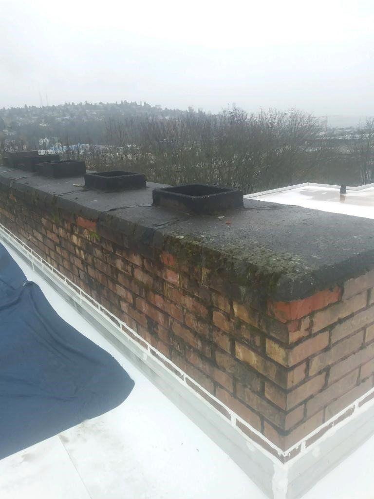 Snowy rooftop with brick chimney, flat black vents, and a gray overcast sky
