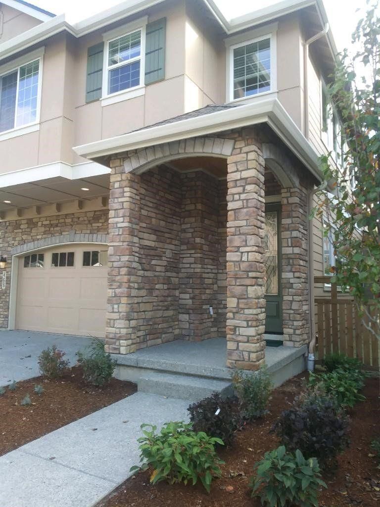 Two-story house exterior with brick entry arch, garage, and front walkway landscaped with shrubs.
