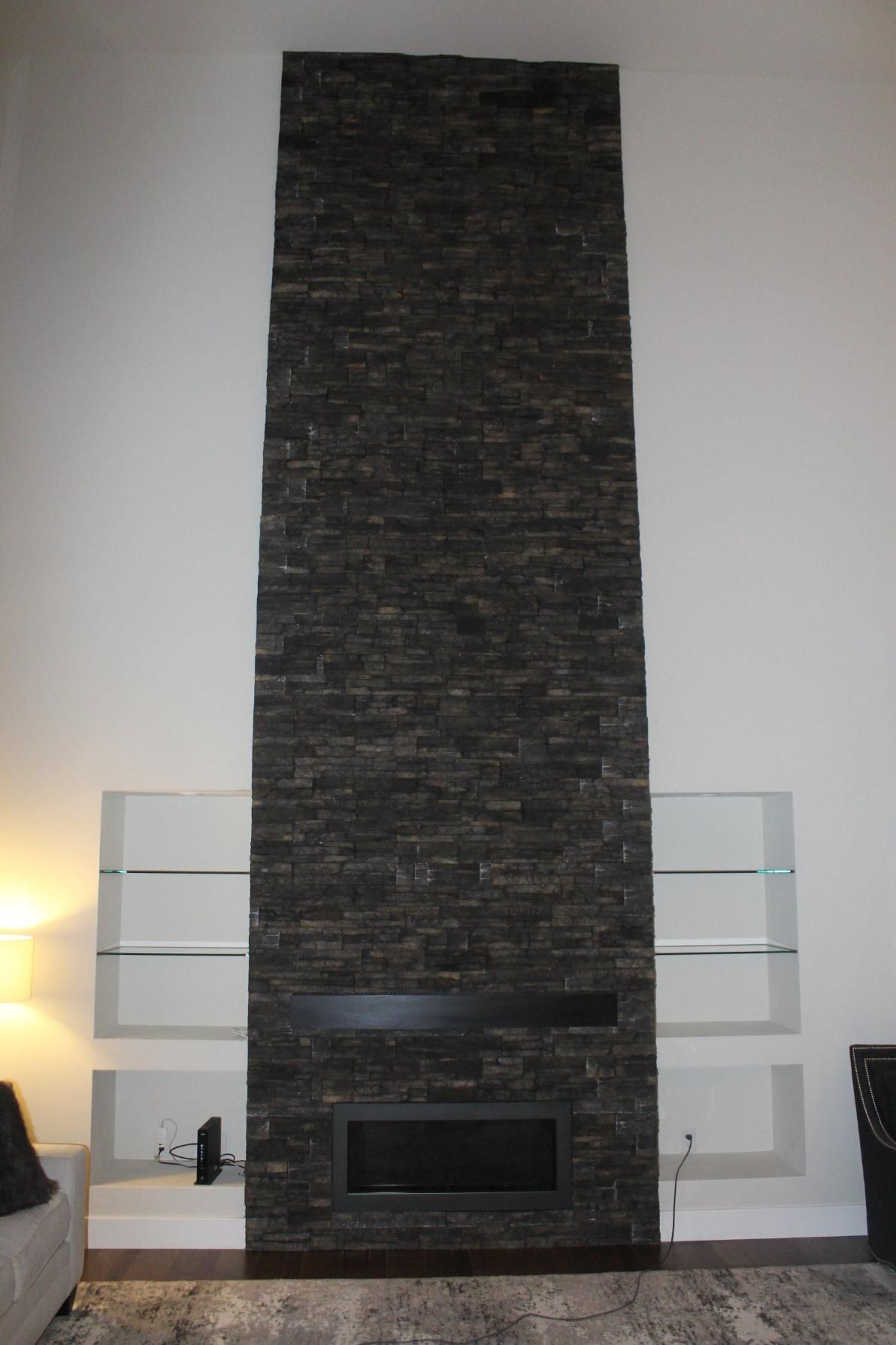 Tall dark stone fireplace with glass shelves in a minimalist living room
