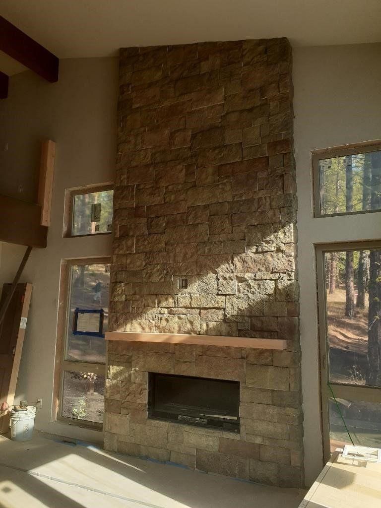 Stone fireplace with mantel in a sunlit room, flanked by narrow windows and a glass door