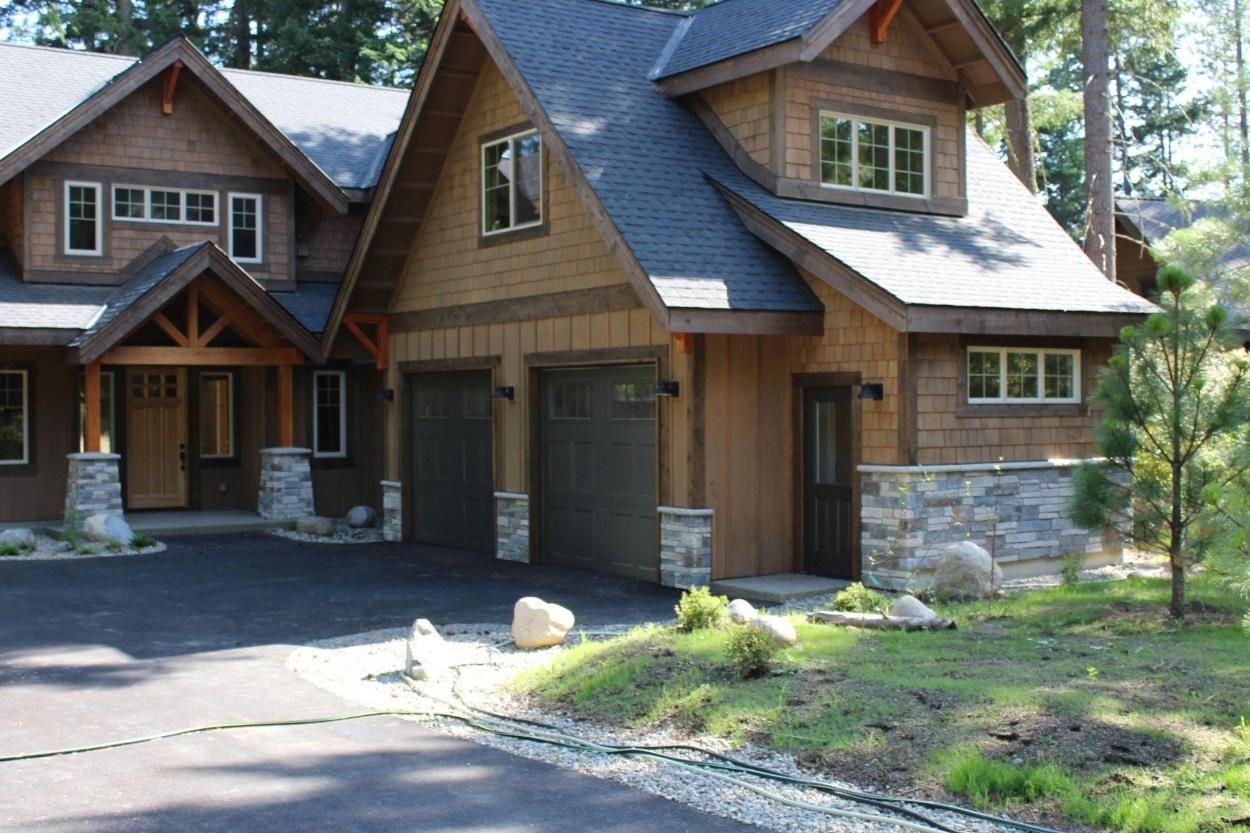 Rustic house with wood siding, stone accents, garage, and a driveway surrounded by trees and lawn