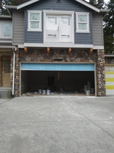 Gray house with an open double garage and stone pillars, viewed from the driveway.