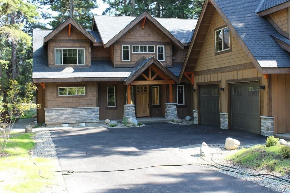 Wooden cabin-style house with stone accents and a large driveway in a forested setting