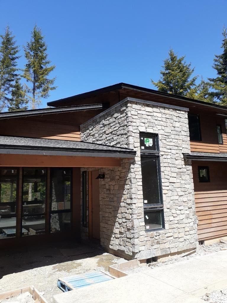 Modern house exterior with stone chimney, wood siding, and large windows under a blue sky