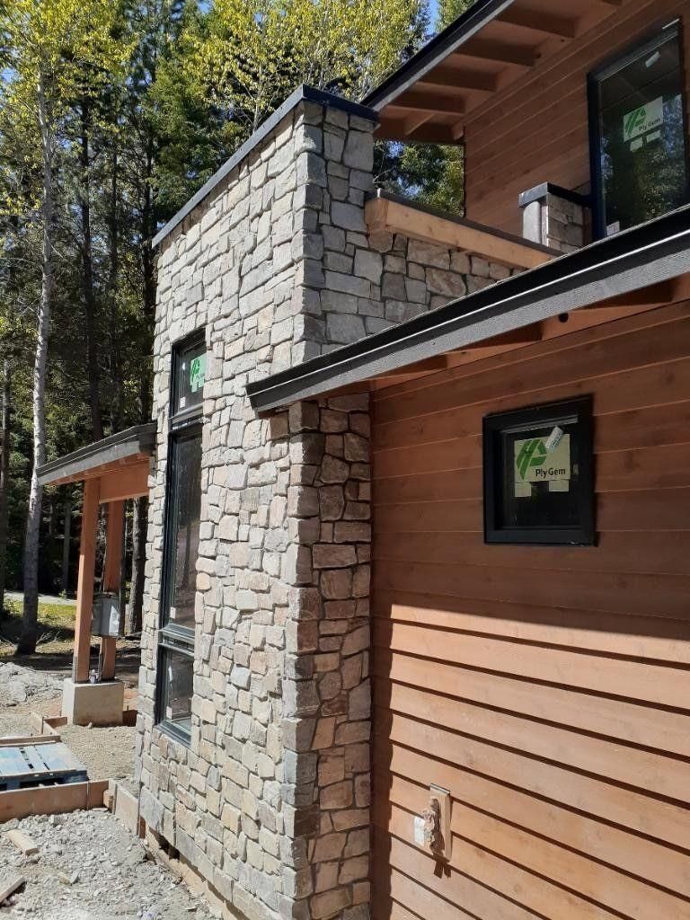 Modern house exterior with stone chimney, wood siding, and covered porch in a wooded setting