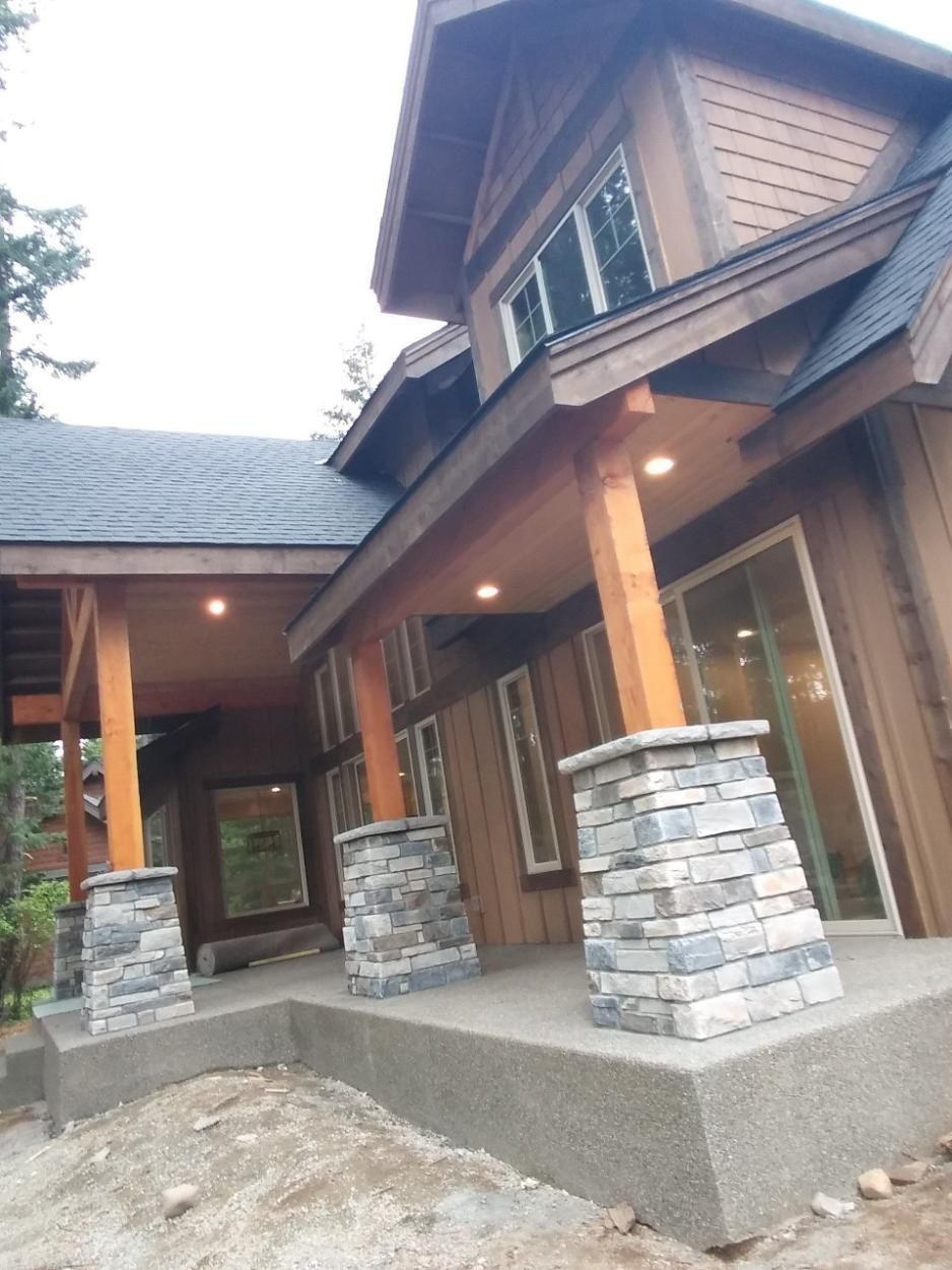 Wooden cabin entrance with stone columns, large windows, and covered porch under construction