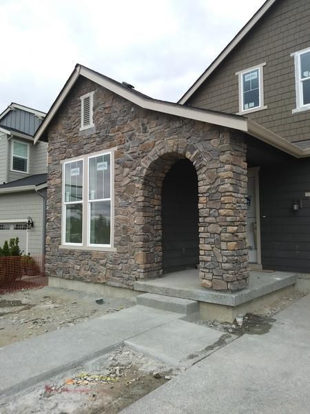 Stone-front house entry with arched porch, large windows, and concrete walkway