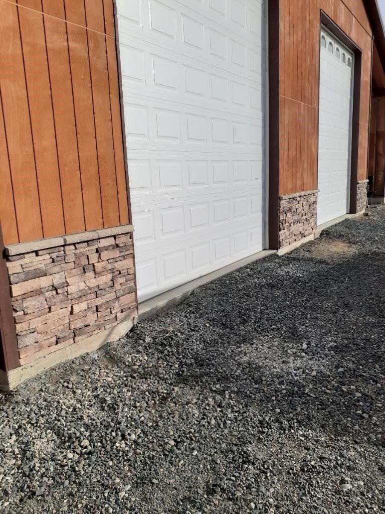 Wood-sided building with white garage doors and a gravel lot in front