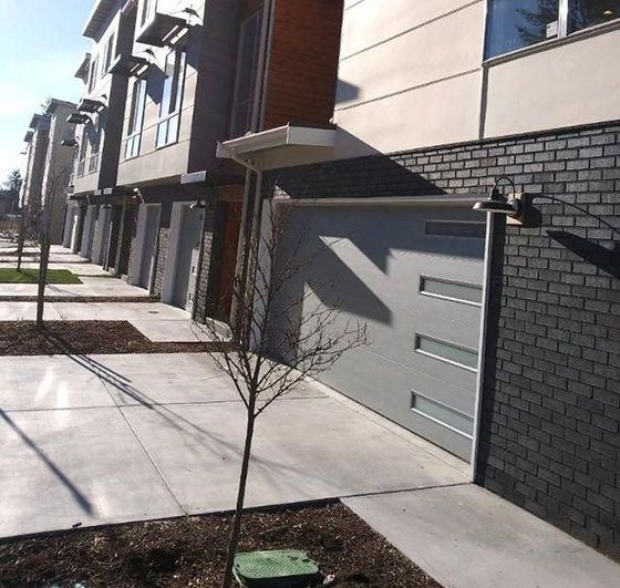 Row of modern townhouses with garage doors, sidewalk, and a young tree in front