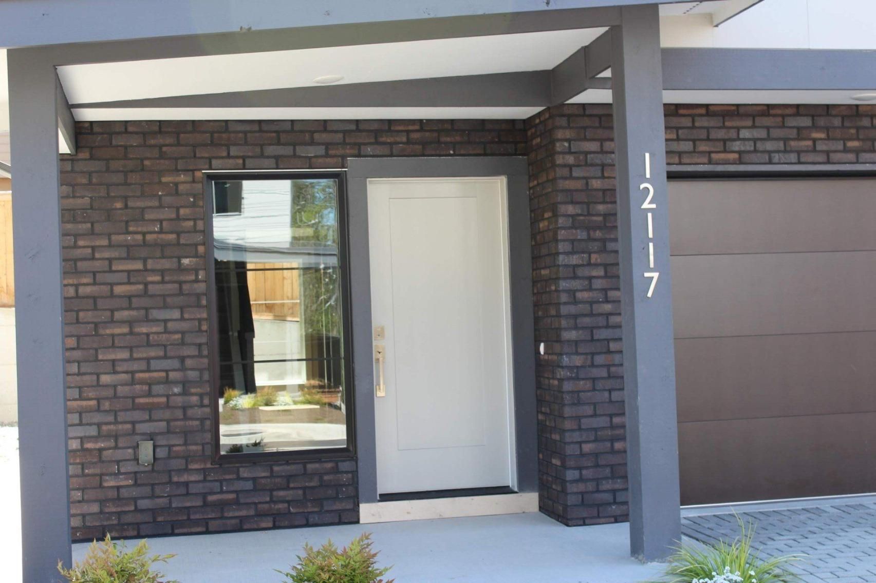 Front entrance of a brick house with a white door, window, and garage, house number 1217 on the pillar