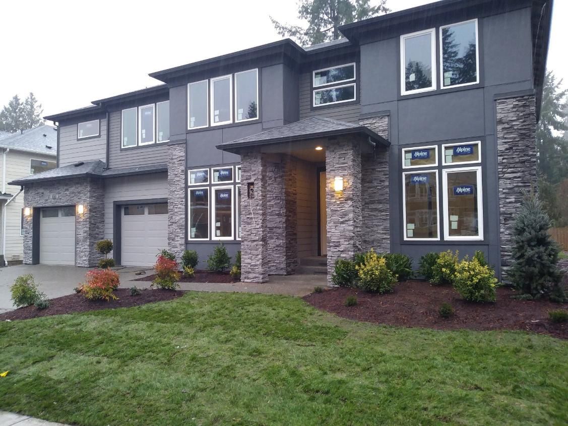 Modern two-story gray house with stone accents, double garage, and landscaped front yard