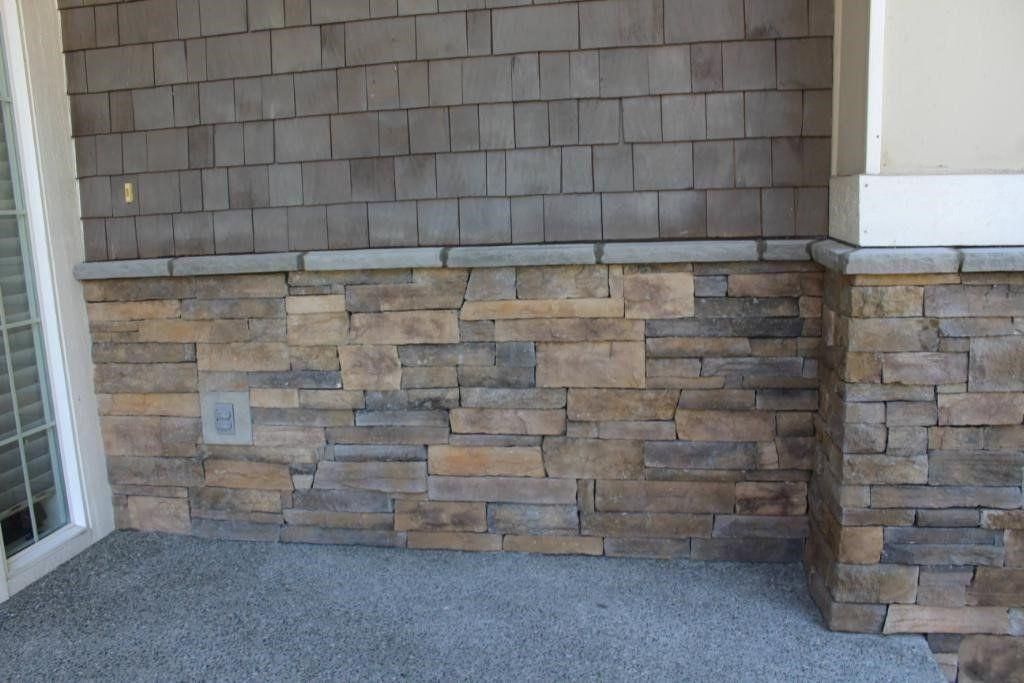 Stone veneer wall on a building exterior beside a window and doorway, with a concrete walkway below.