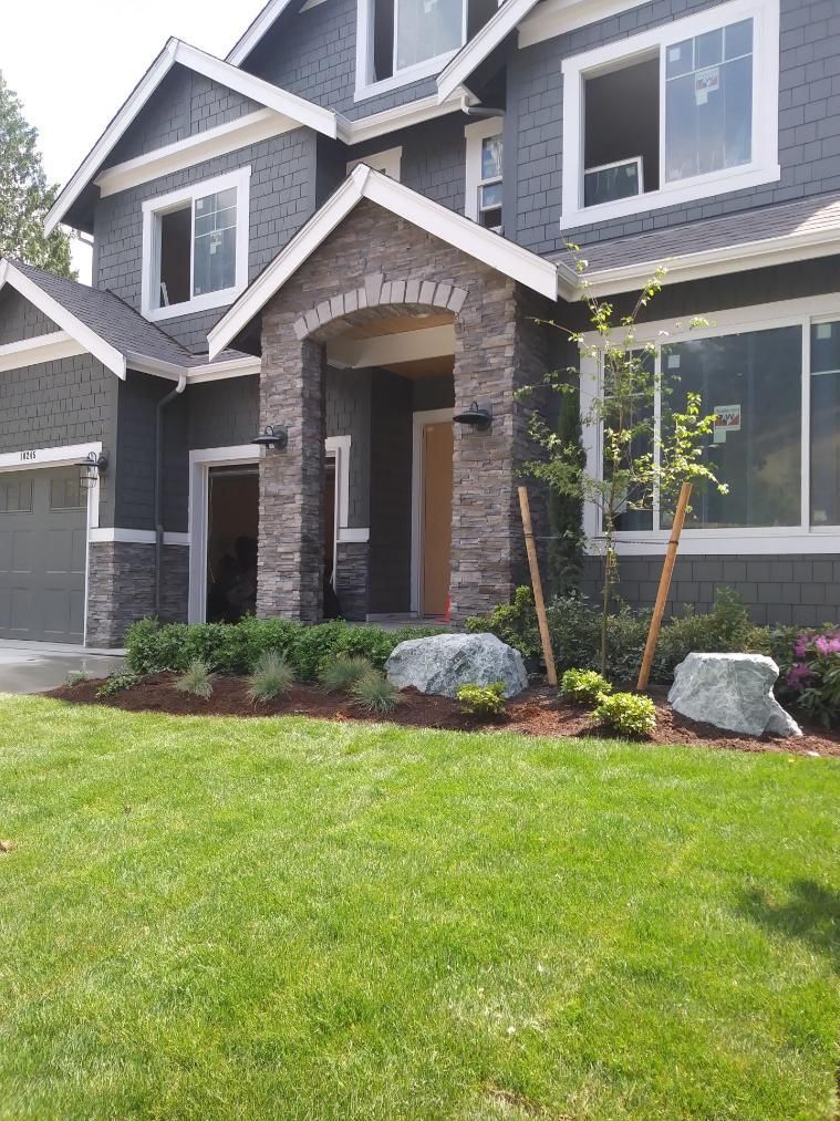 Two-story gray house with stone entry and landscaped front lawn