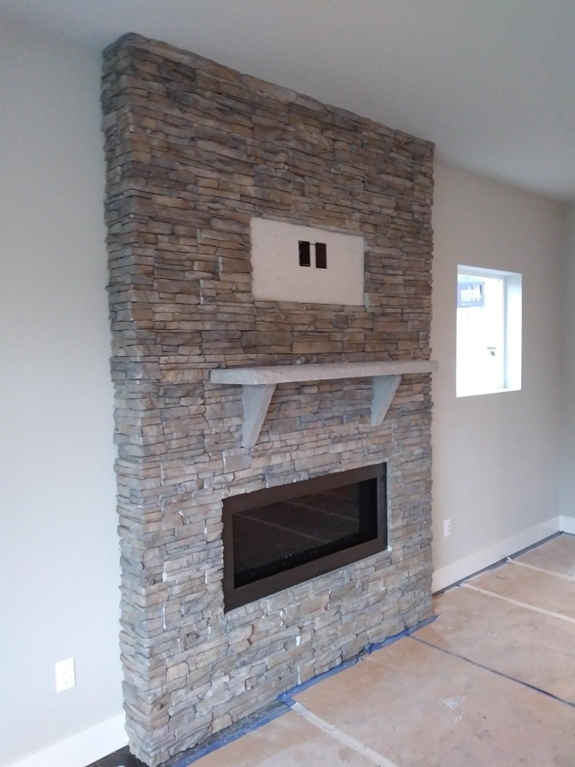 Stone fireplace wall with built-in electric fireplace, shelf, and TV mount in a room under construction
