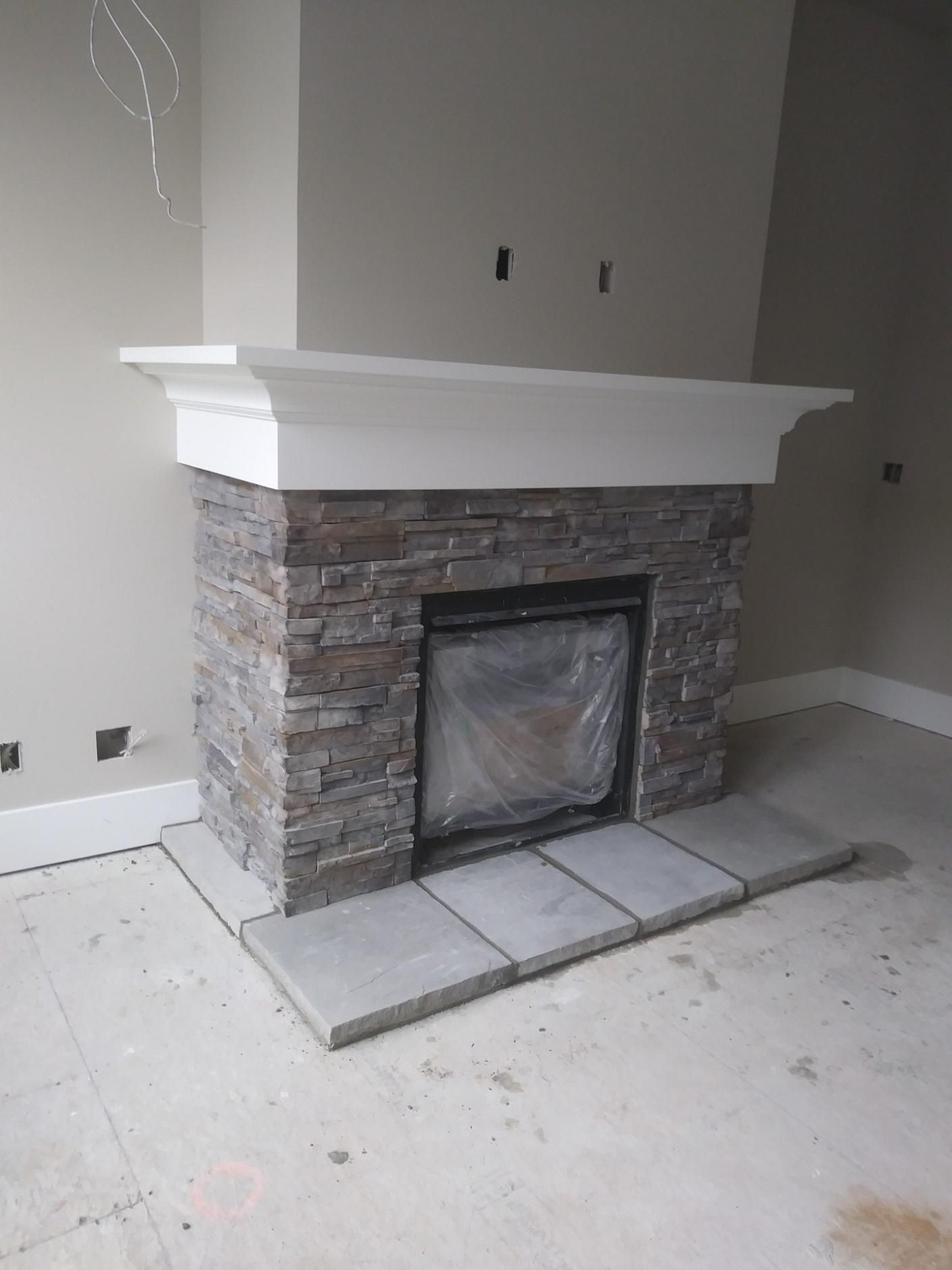 Stone fireplace with white mantel in an unfinished room, with tile hearth and surrounding construction dust