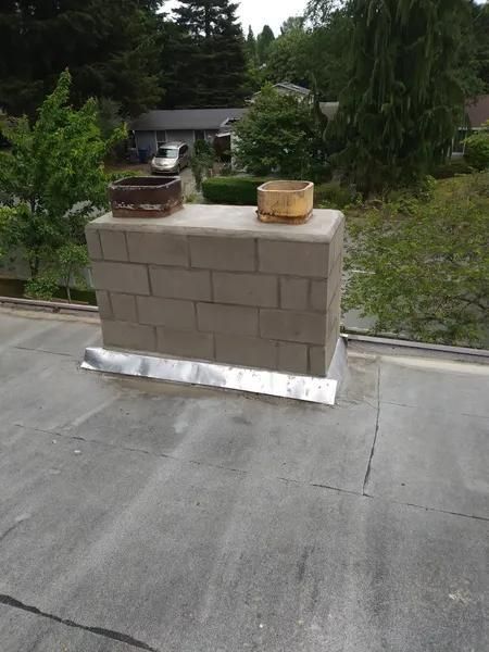 Concrete rooftop vent enclosure with two caps on a flat roof, trees in the background