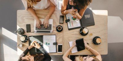 A group of women are sitting around a table with laptops and tablets.