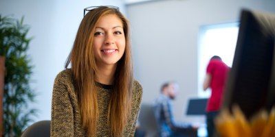 A woman is sitting at a desk in front of a computer and smiling.